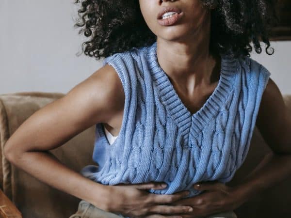 Young African American female sitting on couch at home while having acute pain in stomach